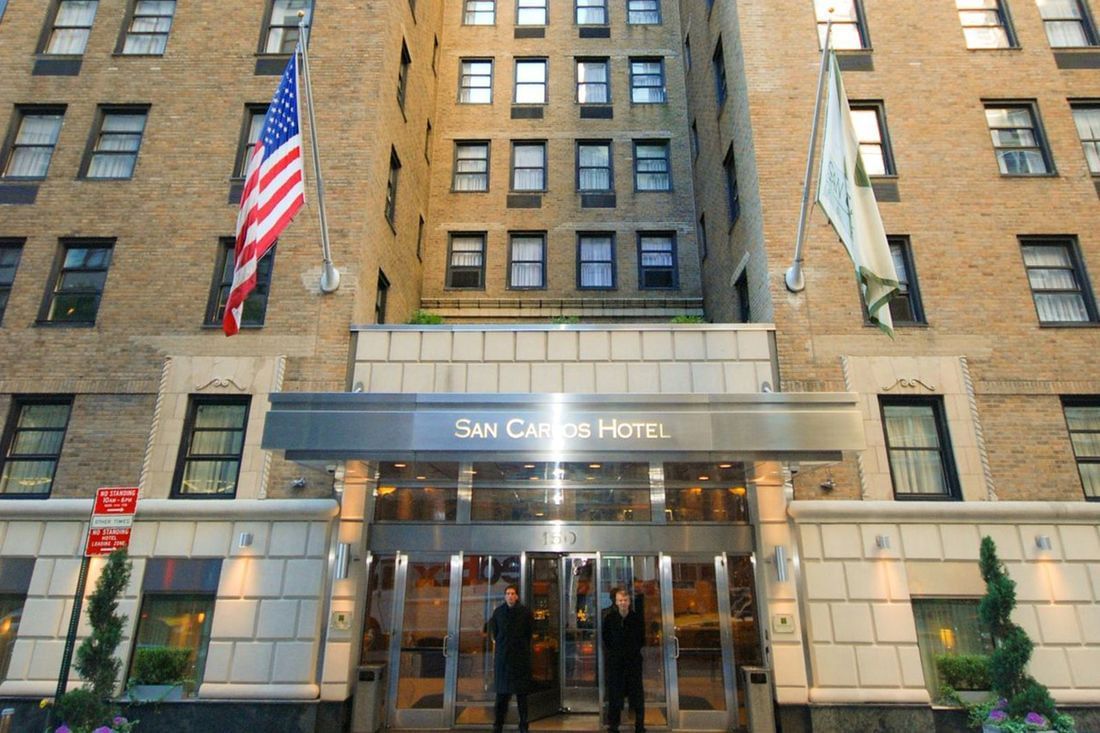 The exterior of the San Carlos Hotel with its entrance, sign, and flags.
