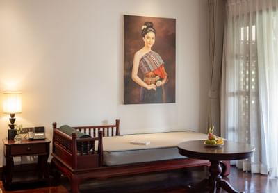 Wooden daybed with round table and Thai women art on the wall in Studio Suite Pondside View at U Luang Prabang