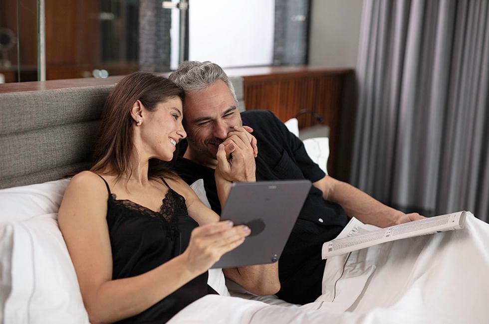 Two people relaxing in bed with a tablet in the room at Live Aqua Resorts and Residence Club