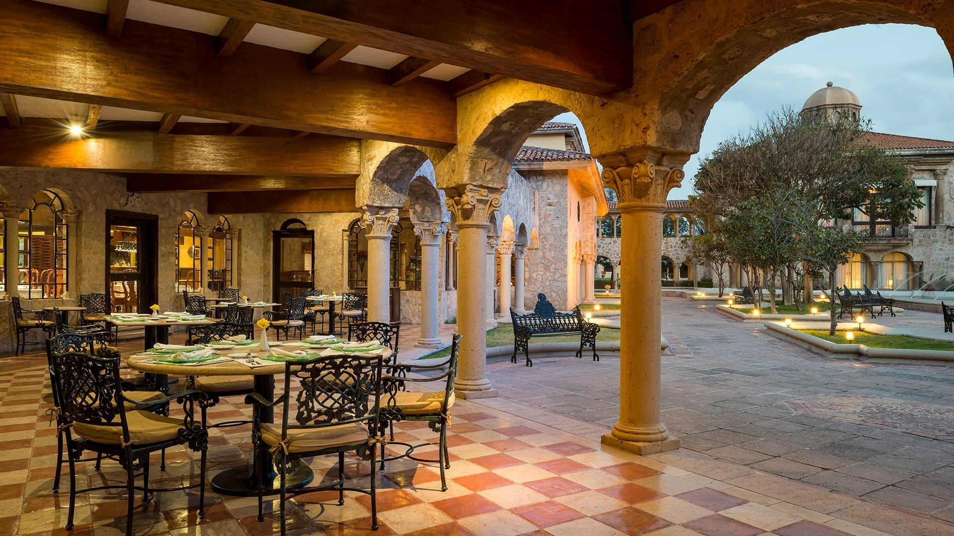 Terraza con arcos coloniales, mesas elegantes y vista al patio iluminado en Tierra Mía, Quinta Real Aguascalientes
