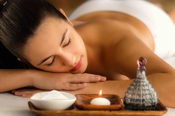 Woman relaxing in spa next to massage oil and beauty product