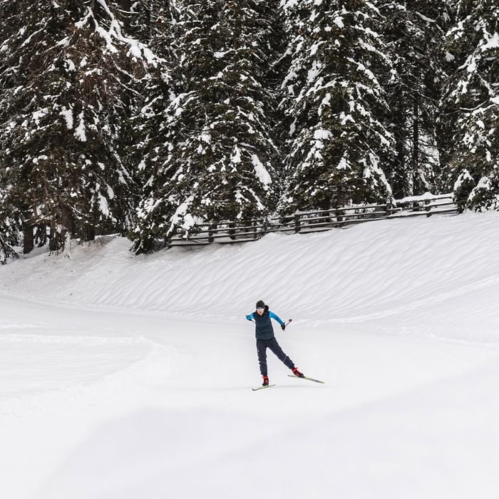 A skier glides through snowy landscape with pine trees at Falkensteiner Hotel Antholz