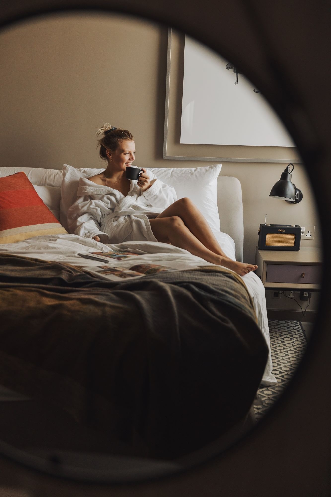 A woman in a bathrobe enjoying a cup of coffee on the bed at The Londoner Hotel