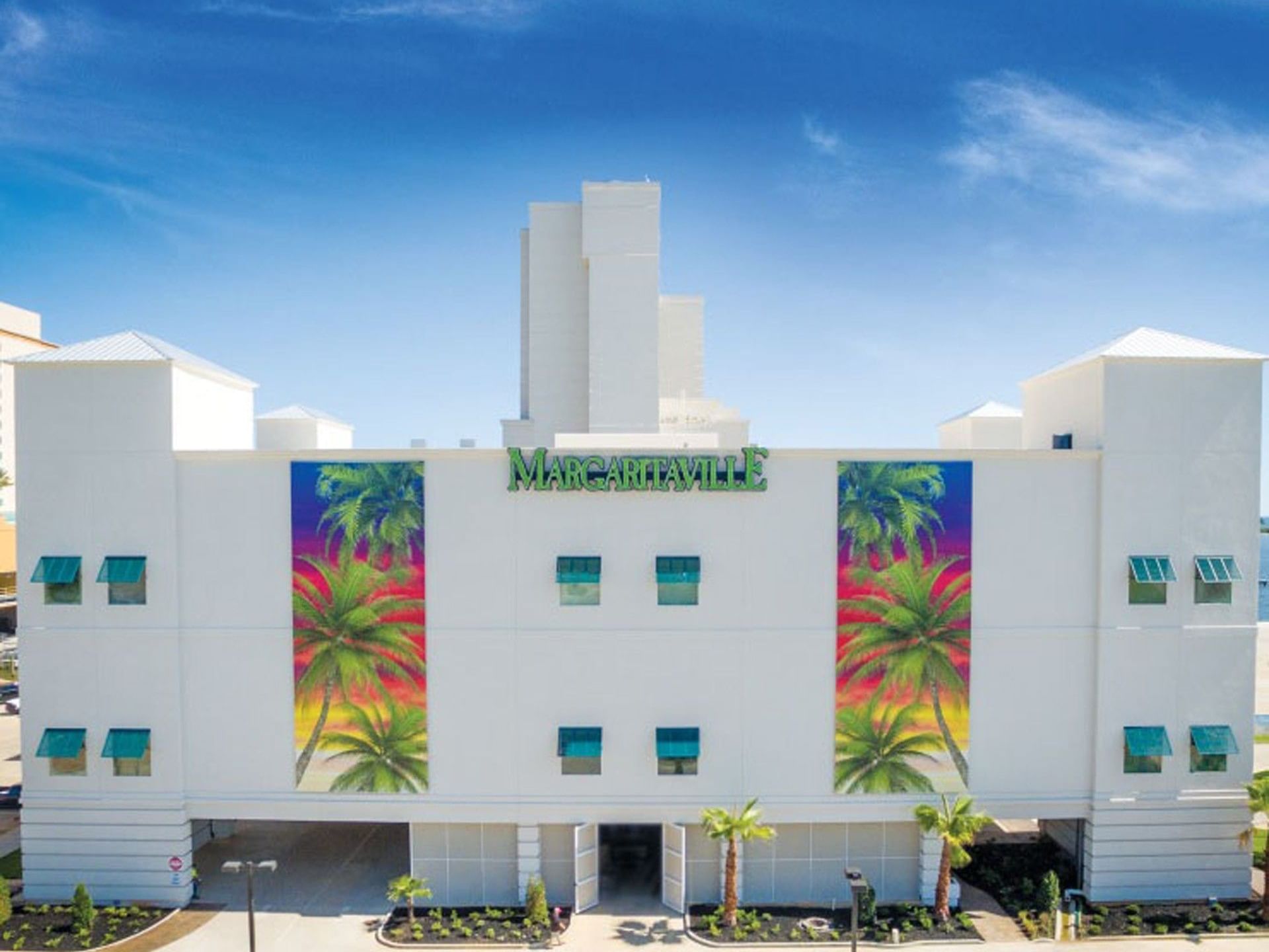 A white Margaritaville Resort Biloxi building near The White House Hotel with palm tree murals and small blue awnings