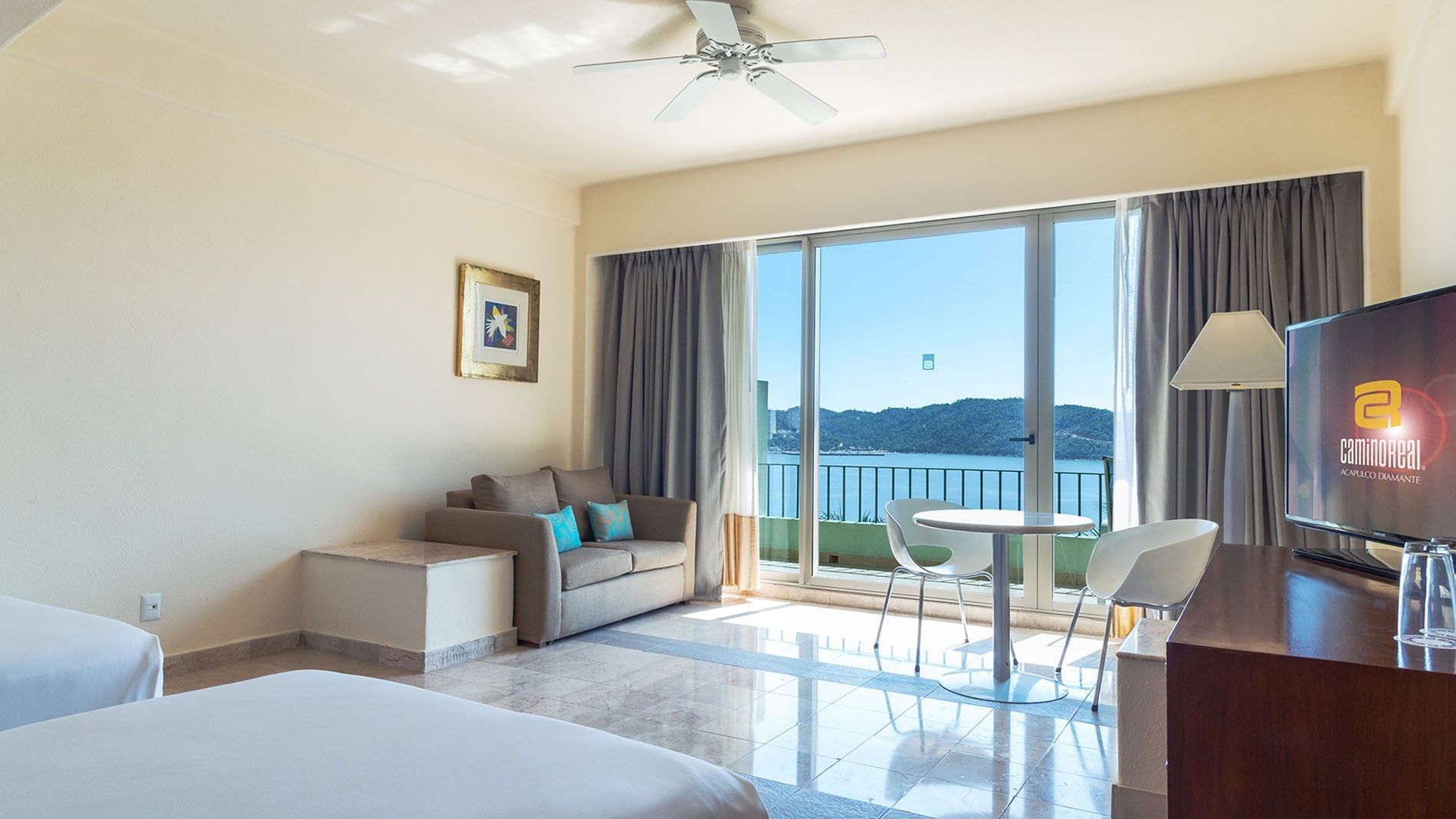 Habitación de hotel con dos camas, sofá, mesa, sillas y balcón con vista al mar.