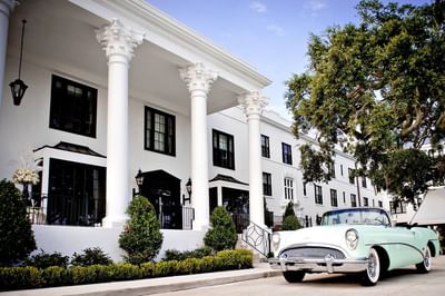 A classic mint car parked outside The White House Hotel, a white building with large columns and green trees