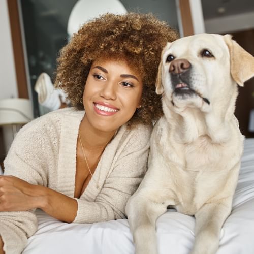 Woman relaxing on a cozy bed with her dog at Rosen Inn Hotels and Resorts