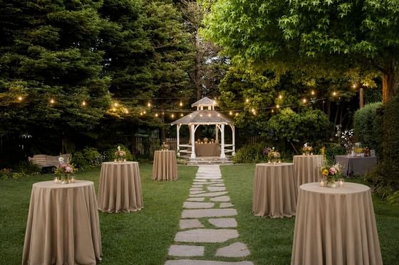 Evening garden reception with white gazebo, string lights, and cocktail tables along stone pathway at Cambria Pines Lodge