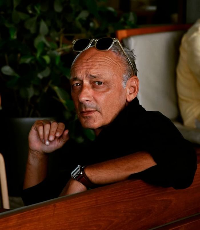 Illustrator Andrea Ferolla, wearing sunglasses, seated with one hand resting on a wooden table at Hotel Motto Vienna