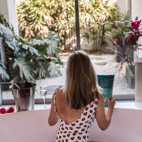 lady relaxing in bath tub with rose petals and reading a book at vie spa central coast