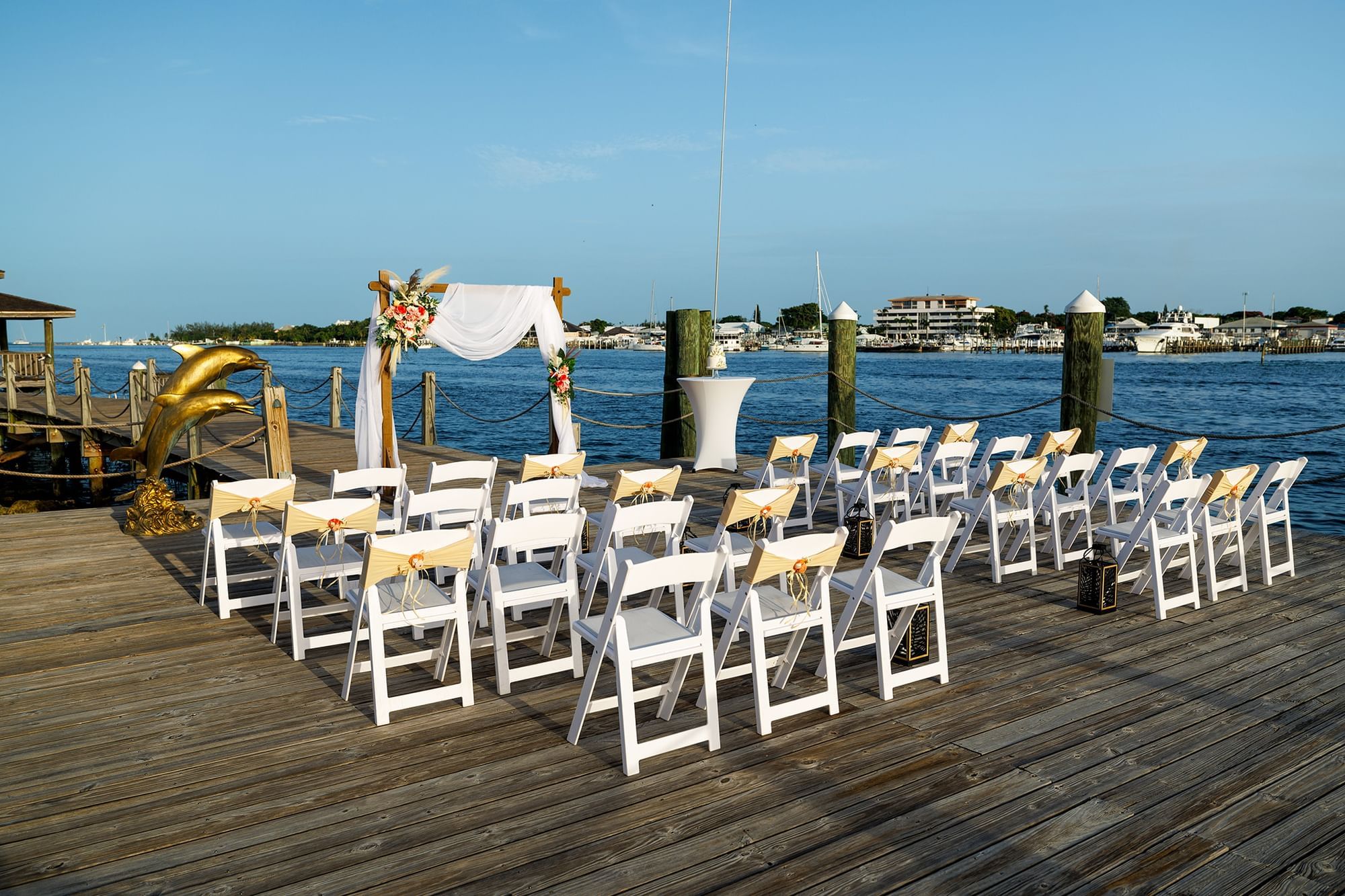 Outdoor wedding setting on a pier with white chairs and an arch overlooking the ocean at Warwick Hotels and Resorts