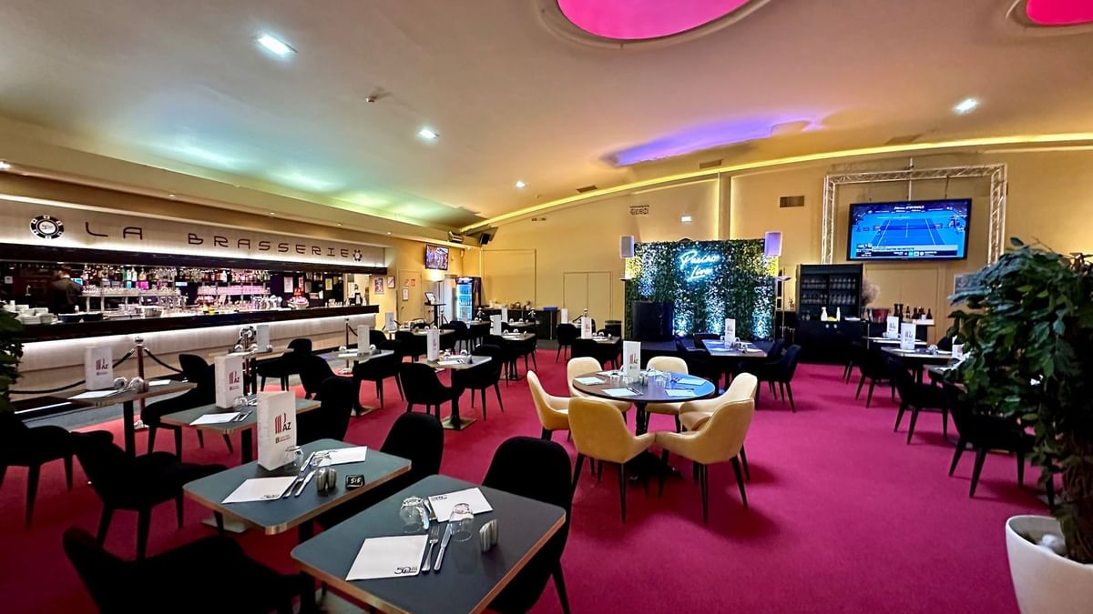 Intérieur d'un restaurant avec tables, chaises, tapis rouge, bar, TV et plantes décoratives.