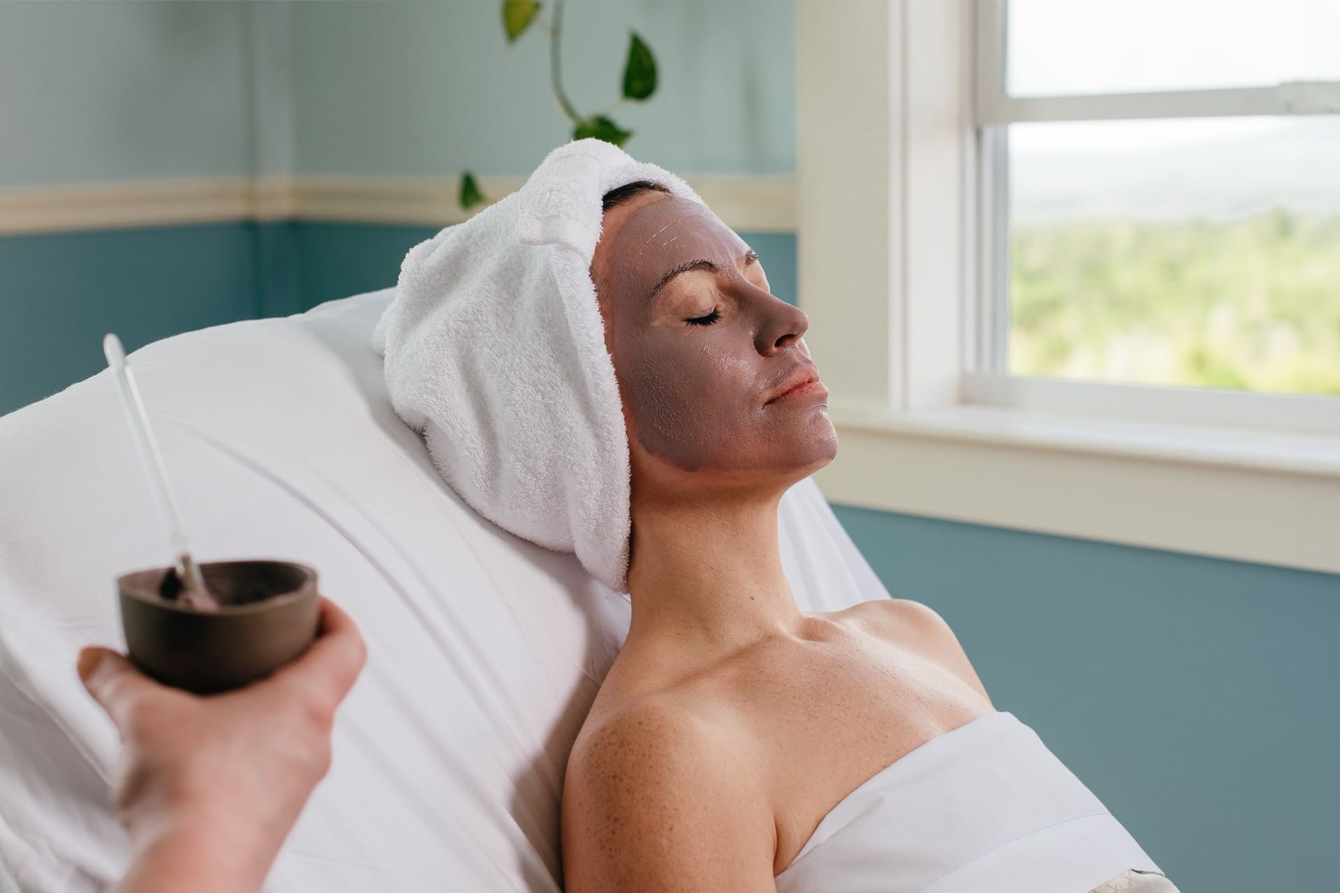 Woman receiving facial mud mask treatment on spa bed beside window at Mountain View Grand Resort & Spa