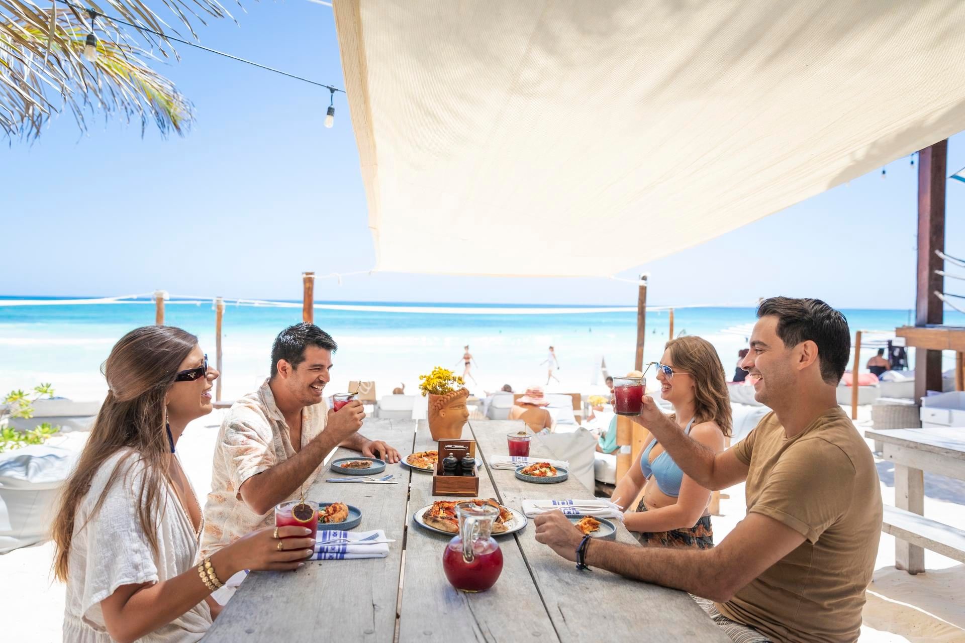 Guests enjoying cocktails and pizza at a rustic outdoor table with a canopy and the ocean view at La Zebra Hotel