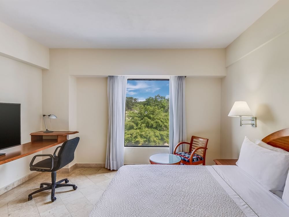 TV & work desk facing king bed with outside view in Accessible Room at Fiesta Inn