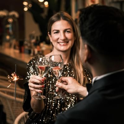 Lächelnde Frau und Mann in eleganter Kleidung stoßen mit Champagner an.