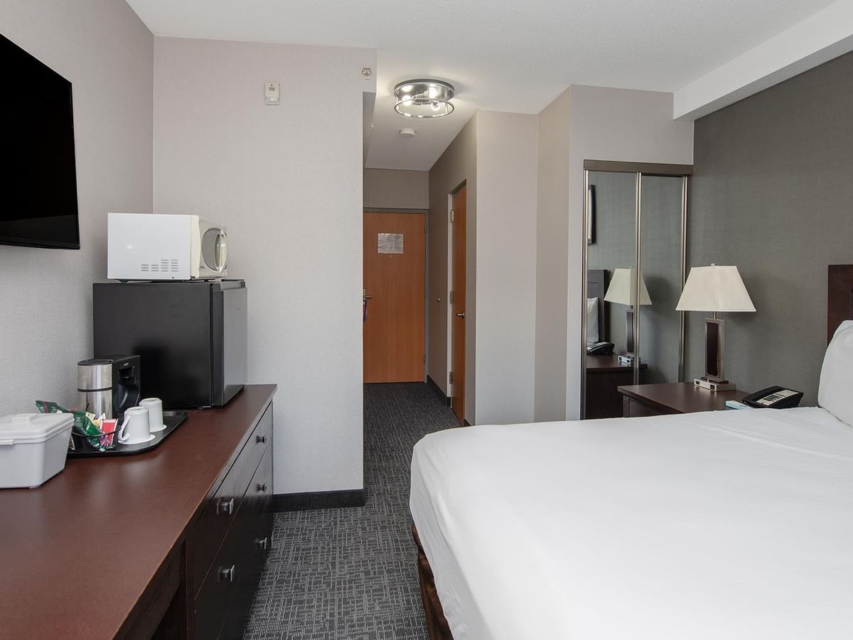 A room with a bed, desk, TV, and mini-fridge.