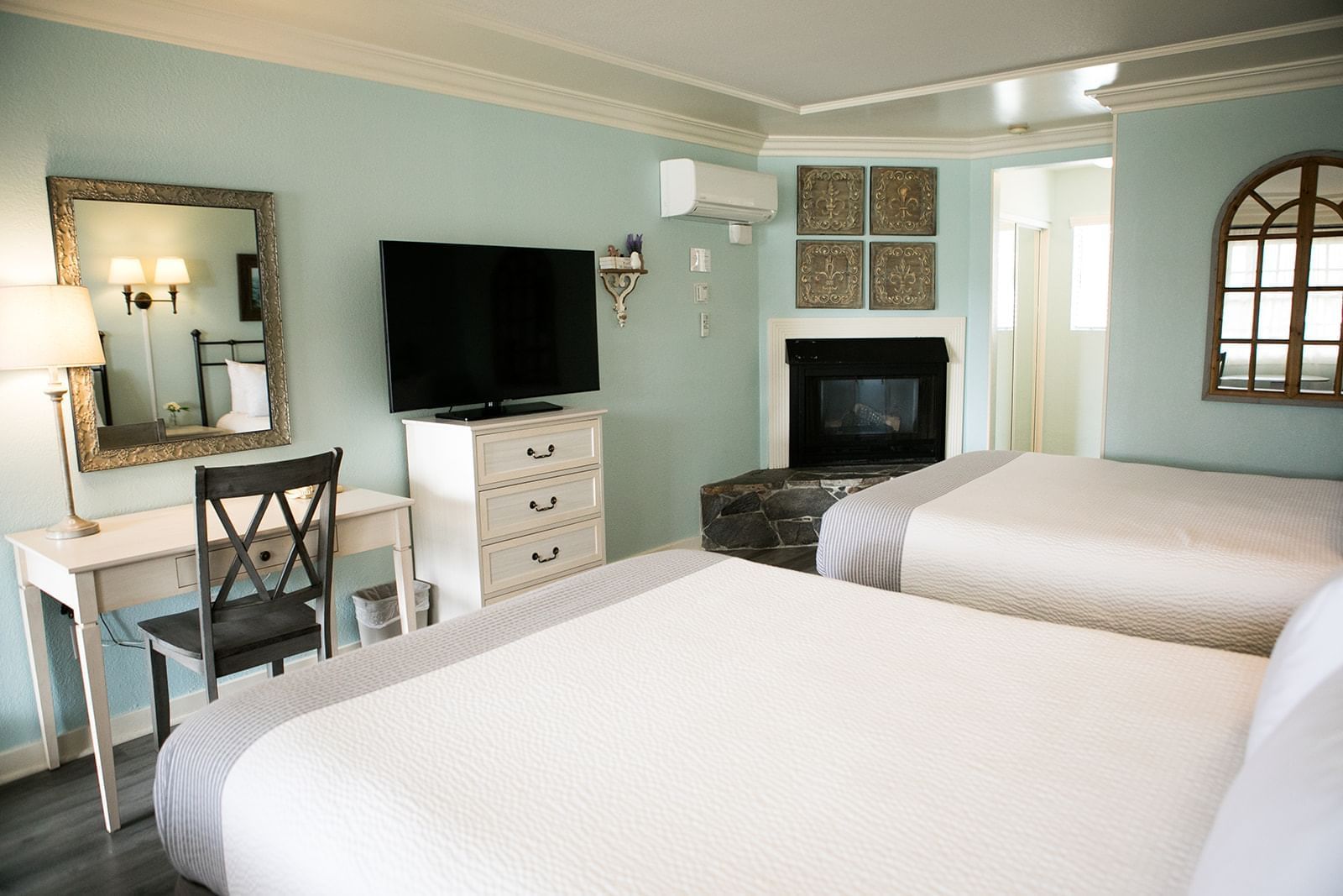 A hotel room with two beds, a fireplace, a TV, a desk, and a mirror.