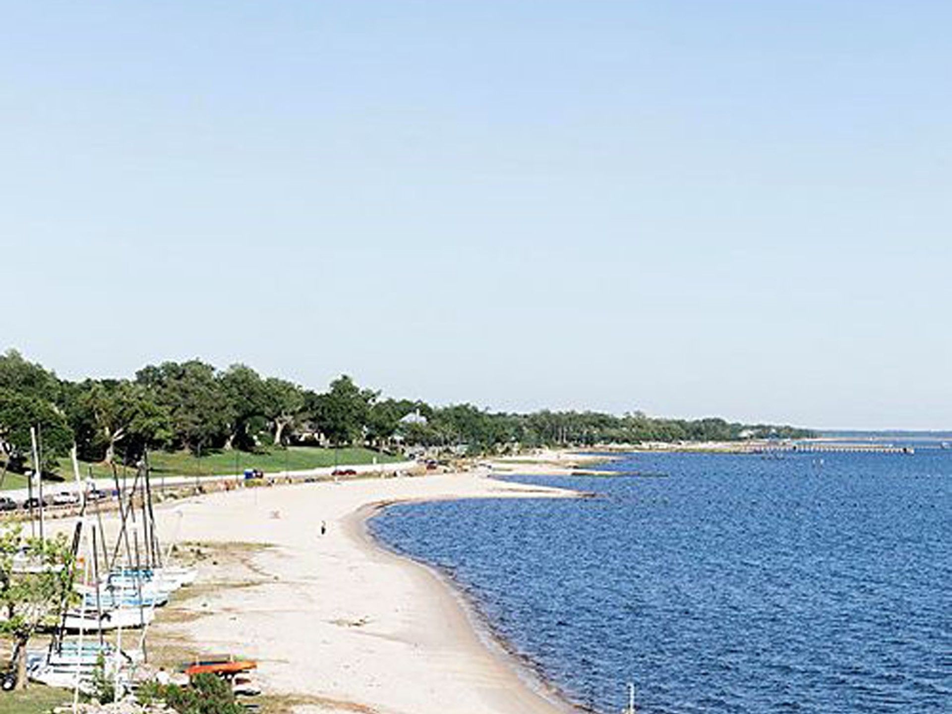 Front Beach in Ocean Springs, near the White House Hotel, curves along blue water with trees and sailboats on the shore