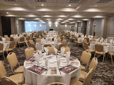 Grand ballroom featuring numerous round tables with place settings and brown chairs at Lake Natoma Inn