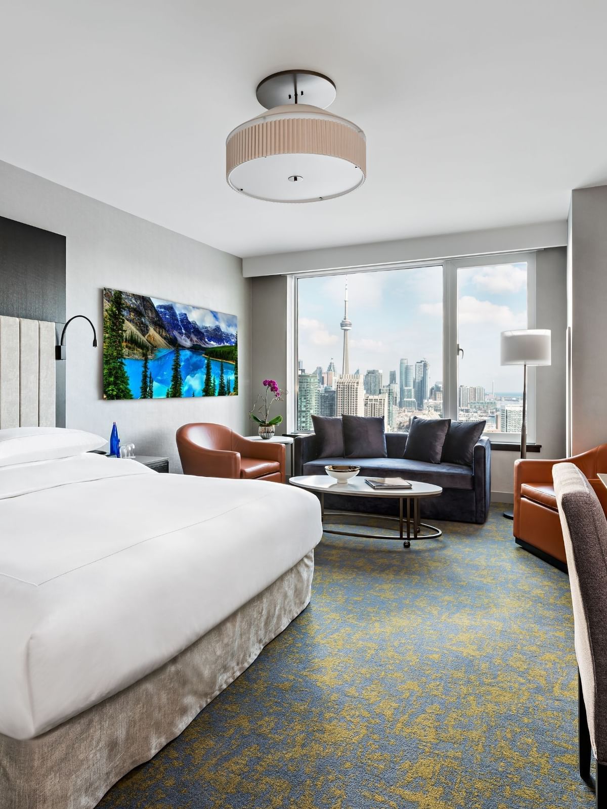 King bed beside dark blue couch and sofa by a large window overlooking the iconic city skyline at Hotel X Toronto