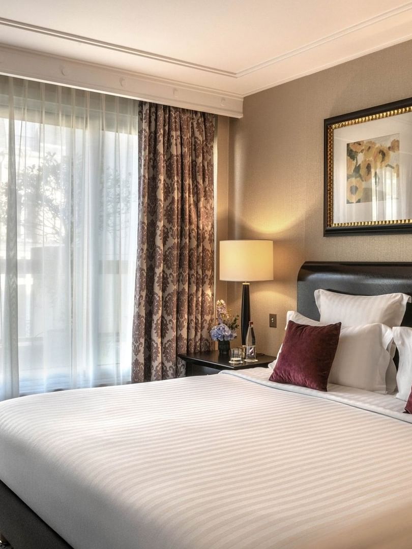 White bed with burgundy pillows by a side table in Elegant Executive Suite with Terrace at Warwick Paris Champs Elysées