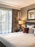 White bed with burgundy pillows by a side table in Elegant Executive Suite with Terrace at Warwick Paris Champs Elysées