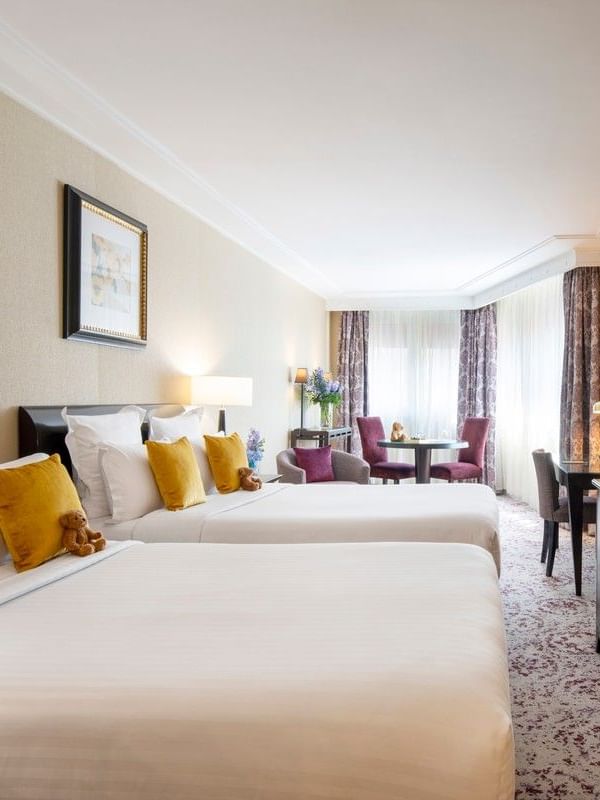 Twin beds with yellow pillows by a TV console in Family room with two queen beds at Warwick Paris Champs Elysées