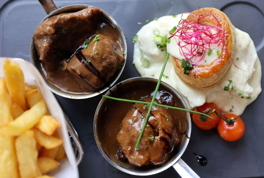 Stoofpot, puree, en friet op een bord in een hotelstijl presentatie.