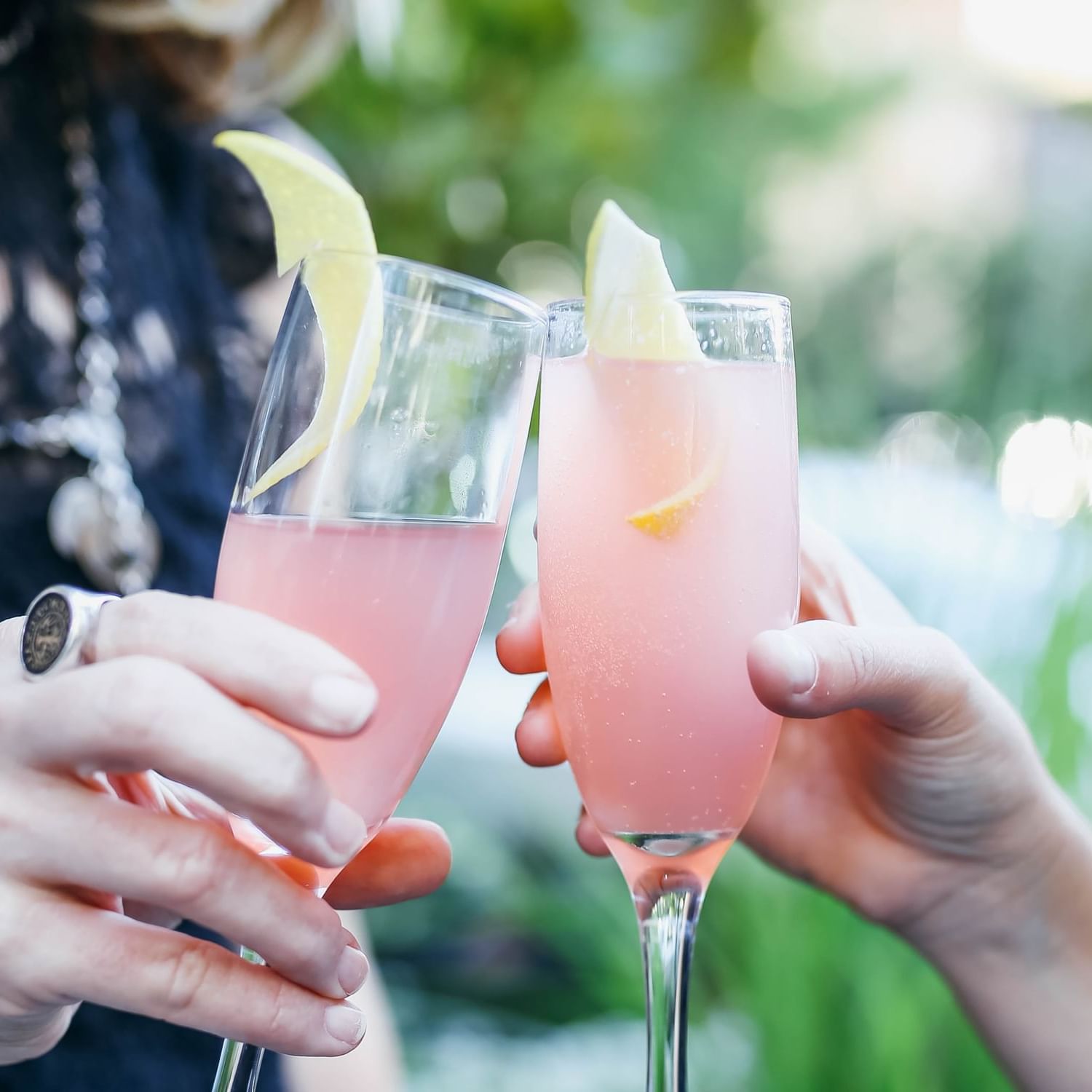 Two people's hands toasting a pink cocktail