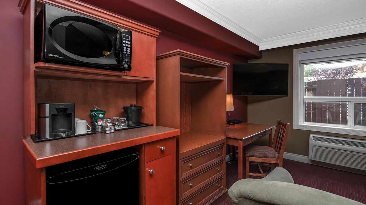 Guest room with wooden kitchenette, microwave, mini-fridge, desk, and wall-mounted TV at Coast Edson Hotel