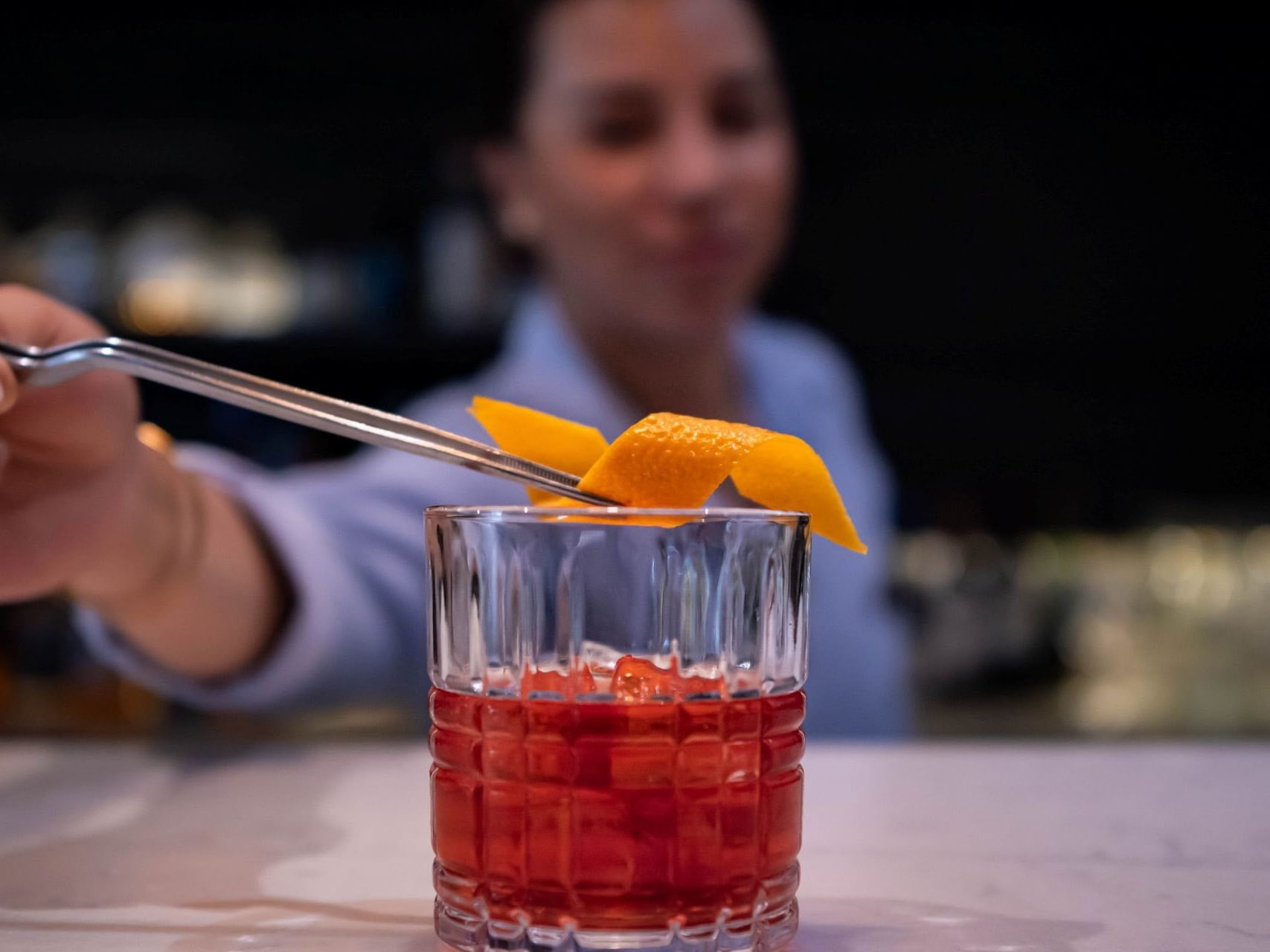 Un camarero decorando un cóctel tinto con una rodaja de naranja en el hotel HCC Costanera Concepción.