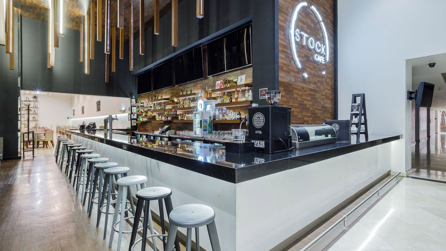 Bar stools by a long white counter under a Stock Cafe sign near the lounge area at Real Inn Tijuana