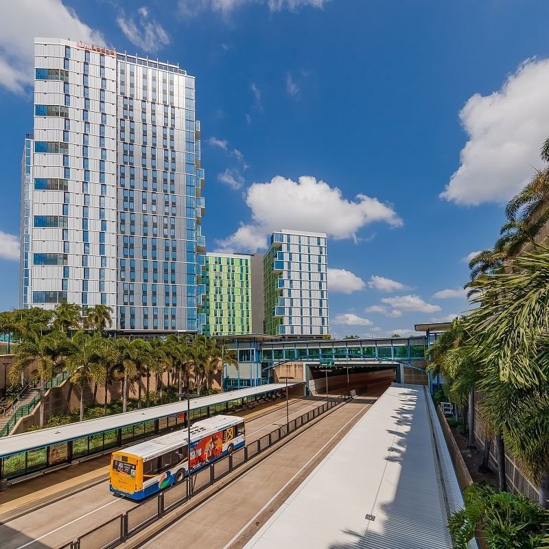 Modern high-rise residential towers with palm trees and a light rail station at UniLodge Park Central under a blue sky.
