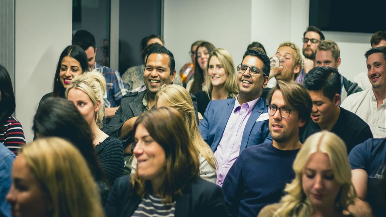 A group of people sitting in a conference room, smiling and engaged during a presentation or event.