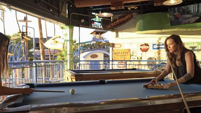 Woman playing pool at an open-air bar with waterfront views at London Bridge Resort