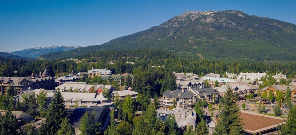 An aerial view of Whistler Village nestled among evergreen forests with mountain slopes in the distance.