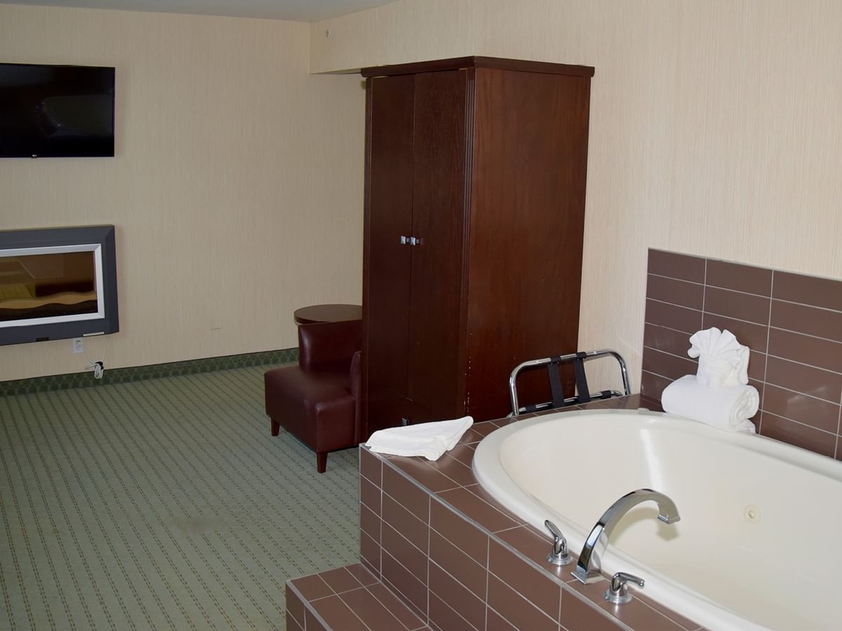 A hotel room with a large bathtub, wooden cabinet, armchair, and TV.
