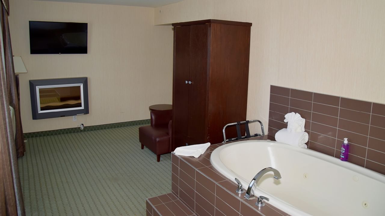 A hotel room with a large bathtub, wooden cabinet, armchair, and TV.