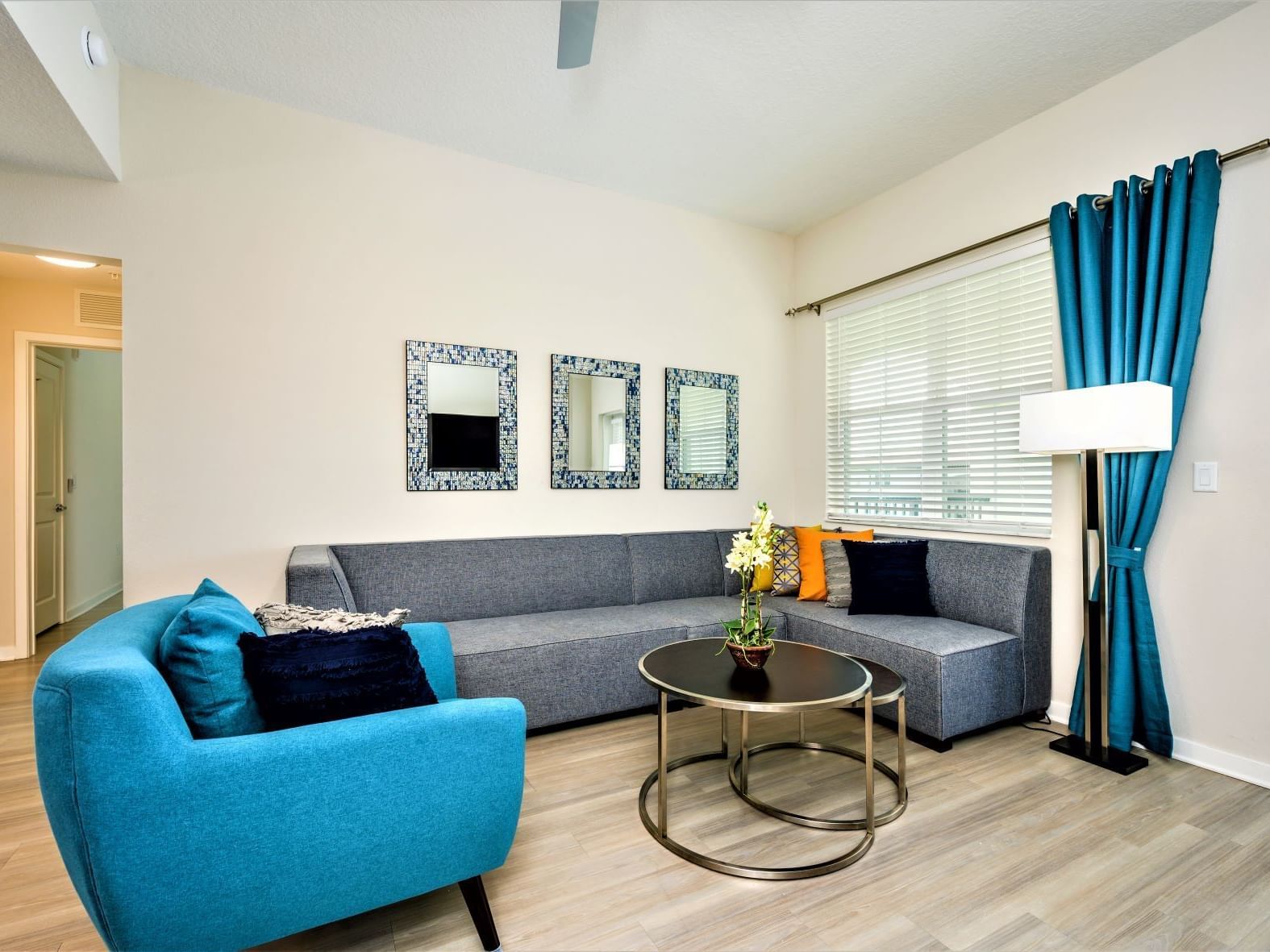 Bright living room with gray sectional sofa, turquoise armchair, and mosaic mirrors at Vista Cay Resort By Millenium