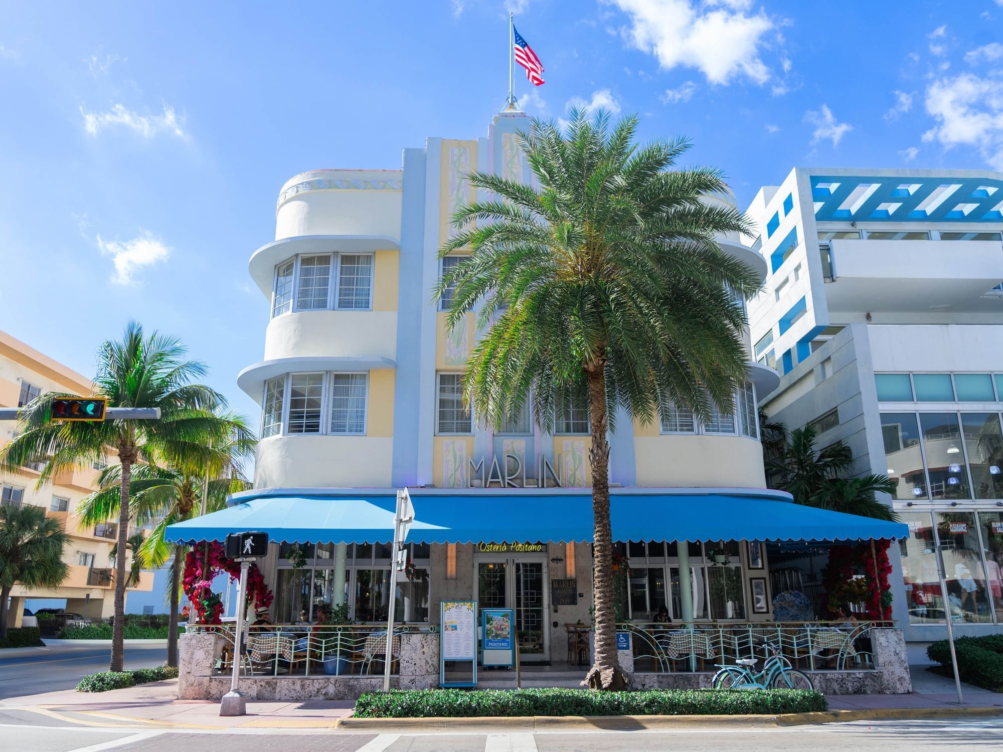 A white and yellow building with a blue awning and a palm tree in front of it.