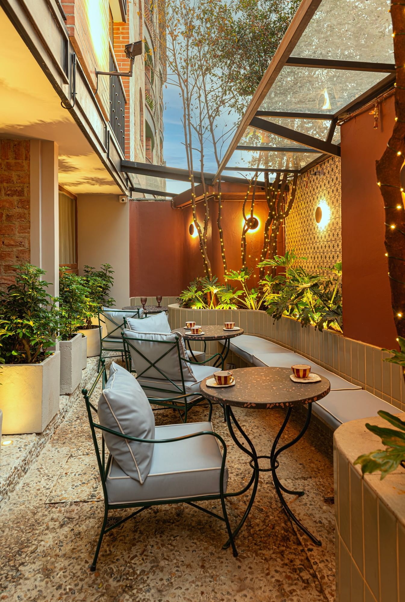 Blue armchairs and round tables under glass roof and fairy-lit trees in the courtyard at 5Q House Chapinero