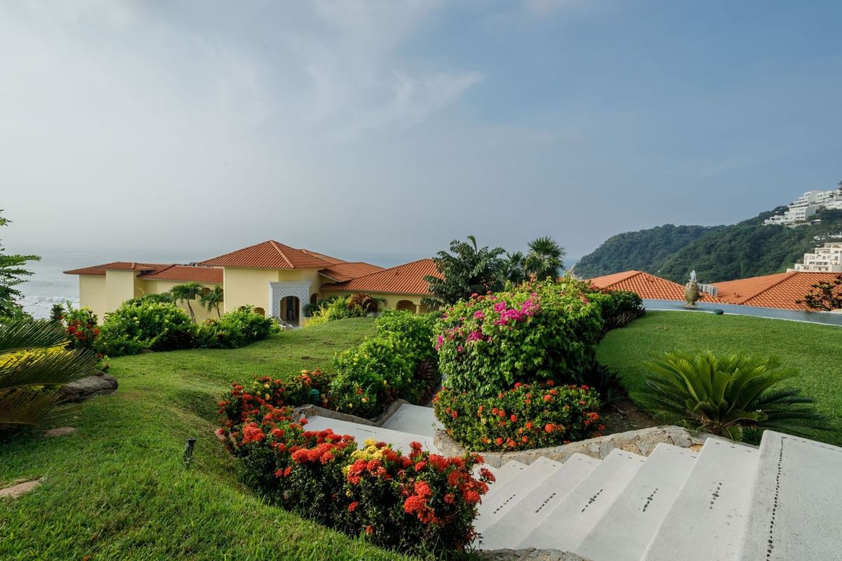 Lush garden steps featuring red flowers and a view of the resort’s tiled roofs at Quinta Real Acapulco
