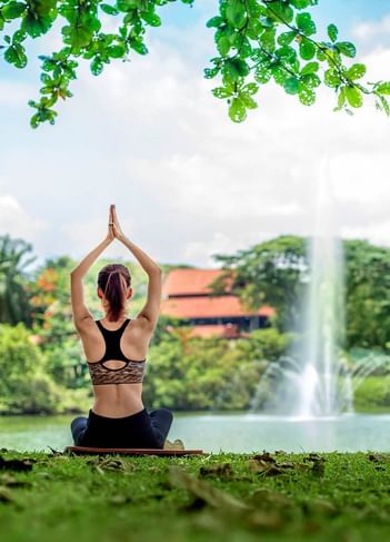 Woman practices yoga outdoors, surrounded by greenery and a fountain at The Saujana Hotel Kuala Lumpur
