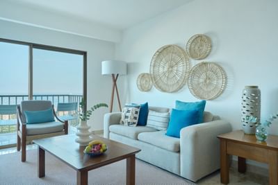 A living room with couch, coffee table, artwork, and balcony with ocean view.