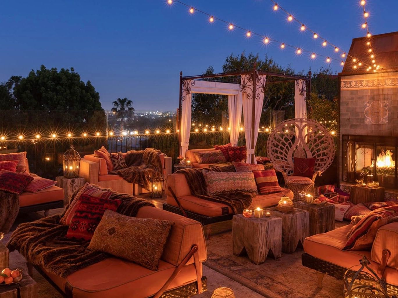 Fire Deck with West Hollywood rooftop lounge with wooden tables under string lights and a fireplace at Petit Ermitage