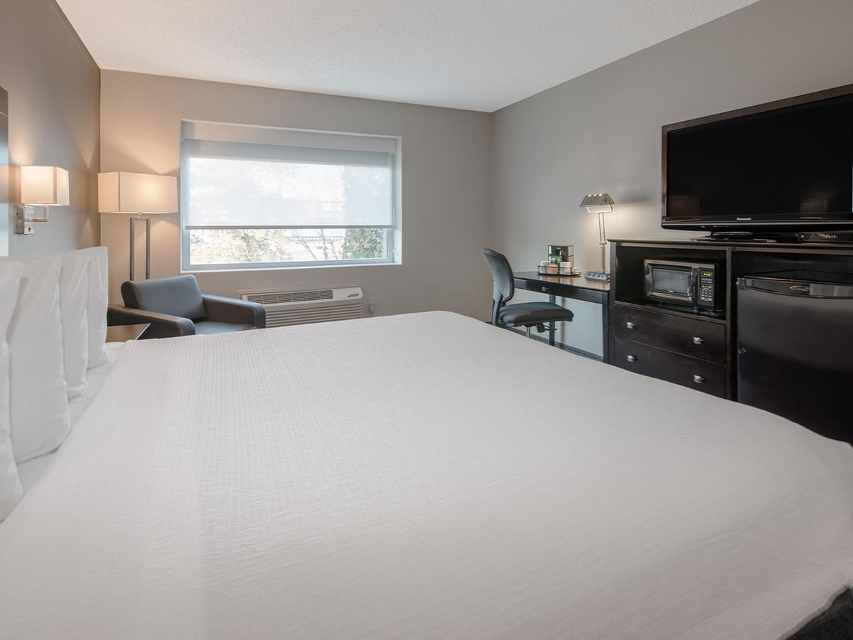 King-sized bed with white bedding, desk, chair, and TV.