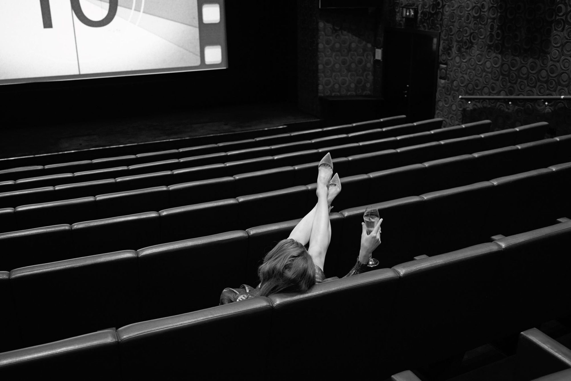 Woman with glass relaxing in movie theater at The May Fair Hotel, London.