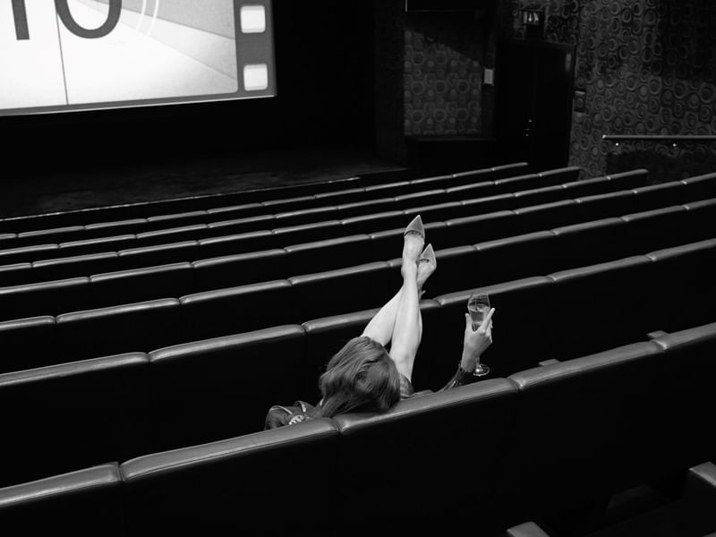 Woman with glass relaxing in movie theater at The May Fair Hotel, London.