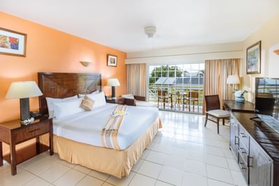 Spacious room with a king-size bed, warm orange walls, and large windows in Jr Executive Suite King at Bay Gardens Hotel